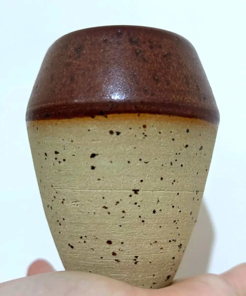 Vaso de gres claro con motas oscuras y la boca esmaltada en marrón brillante.