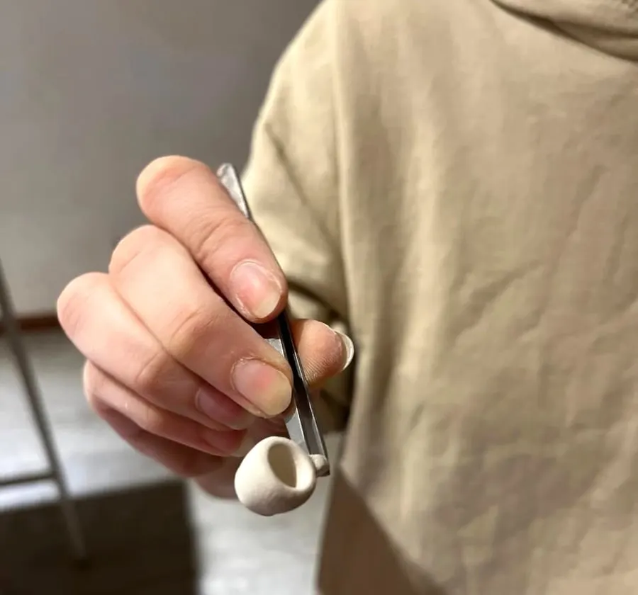 Una tacita miniatura sostenida con una pinza.